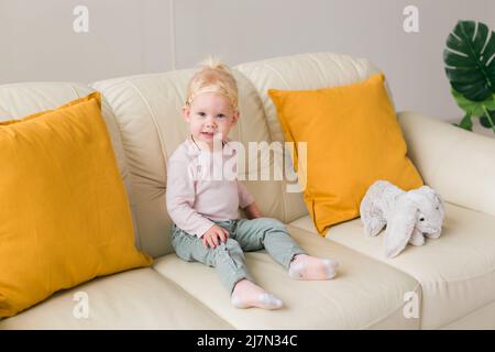 Bambina con impianto cocleare seduta sul divano a casa. Ascolta il concetto di comunità dei non udenti e dei non udenti Foto Stock