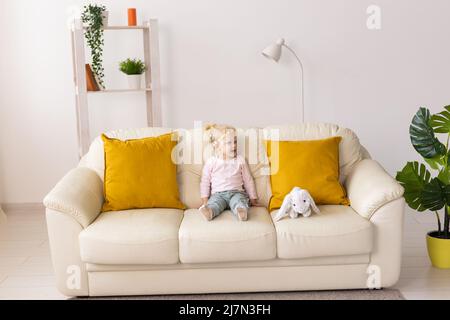 Bambina con impianto cocleare seduta sul divano a casa. Ascolta il concetto di comunità dei non udenti e dei non udenti Foto Stock