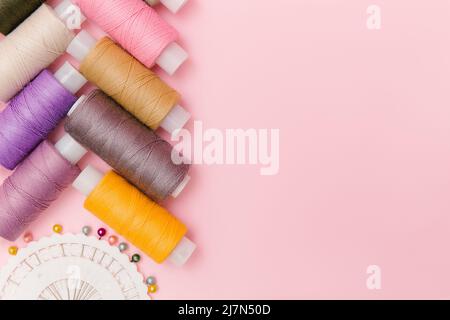 Strumenti da cucire e accessori da cucire su elegante sfondo rosa. Medicazione, sfondo su misura. Fili da cucire multicolore, spole di fili, aghi, perno Foto Stock