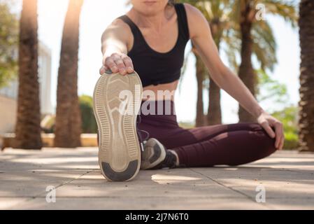 Donna sportiva fuori scaldarsi esercizio con le gambe allungate Foto Stock