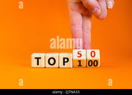 Dal simbolo Top 100 al 50. Businessman trasforma i cubi di legno e cambia le parole di concetto Top 100 to Top 50. Bella tavola arancione e sfondo. Affari Foto Stock