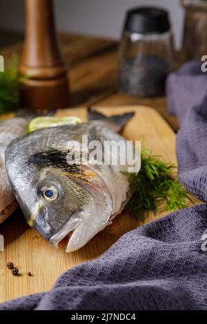 Pesce dorado sbucciato crudo con ingredienti da cucina. Pesce fresco su sfondo di legno. Foto Stock