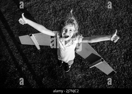 Eccitato divertente bambino ragazzo che vola in aereo fatto di ali di cartone. Sogno, immaginazione, infanzia. Ragazzo sogna di volare. Bambino che gioca senza preoccupazioni Foto Stock