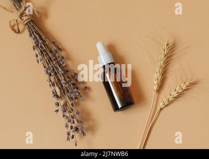 Siero in bottiglia di vetro con lavanda e altri fiori secchi su sfondo beige Foto Stock