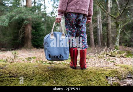 bambino che tiene in mano una borsa per pranzo al sacco mentre cammina nella foresta Foto Stock