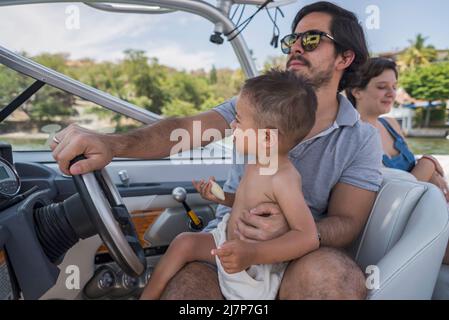 Giovane padre che porta suo figlio a vela guidando una barca seduta Foto Stock
