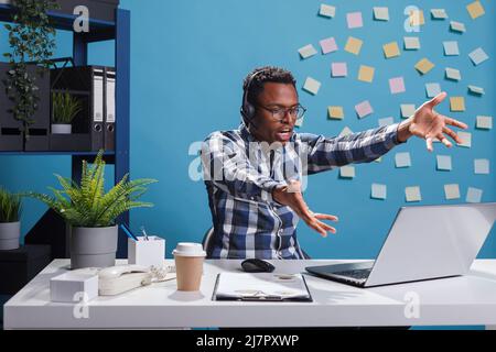 MAD arrabbiato operatore call center urla con rabbia mentre parla con il cliente. Un agente di telemarketing furioso urla sul laptop mentre punta aggressivamente allo schermo nello spazio di lavoro dell'ufficio. Foto Stock