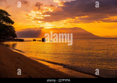 Tramonto caldo con silhouette di montagne sulla spiaggia e oceano tranquillo Foto Stock