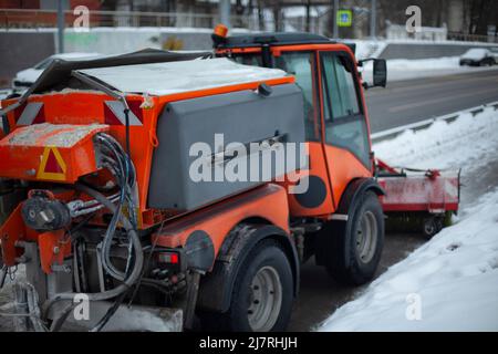 Rimozione della neve in città. L'attrezzatura speciale pulisce la strada. Spazzole di trasporto arancioni per la rimozione della sporcizia dalla strada. Lavoro dei servizi pubblici in Russia. Foto Stock