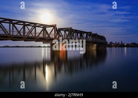 La luna piena che sorge su un vecchio ponte ferroviario. Fotografato al porto di Tauranga, Tauranga, Nuova Zelanda Foto Stock