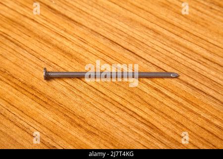 Ferro di metallo chiodo molto appuntito su legno di noce in, isolato su sfondo di legno Foto Stock