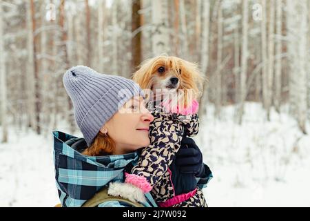 Cane cinese in purrebred crested con il suo proprietario in inverno all'aperto. Donna e cane in abiti caldi inverno godere di una passeggiata nella foresta. Spazio di copia Foto Stock