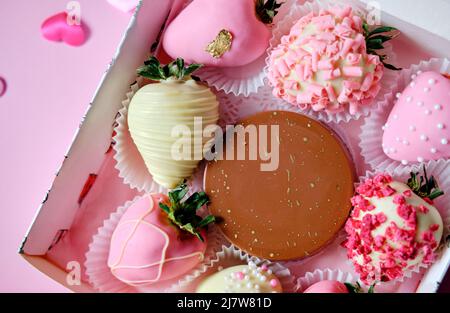 fragole in cioccolato in scatola con cuori sparsi su sfondo rosa. Dolce regalo per San Valentino Foto Stock