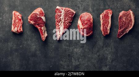 Varietà di bistecche di manzo su sfondo scuro. Fette di carne cruda Foto Stock