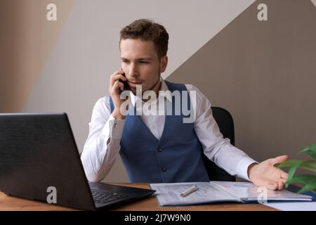 Foto riuscito uomo focalizzato con barba e utilizza moderno digitale smart dispositivo parlare, chattare sui social network, tastiere su un computer portatile, leggere notizie su siti web, lavorare in un ufficio Foto Stock