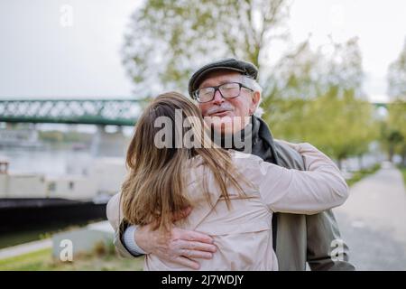Vista posteriore della figlia adulta che abbraccia il padre quando lo incontra all'aperto in strada. Foto Stock