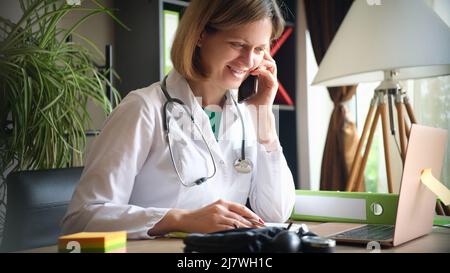 Sorridente medico che parla al telefono sul posto di lavoro in clinica Foto Stock