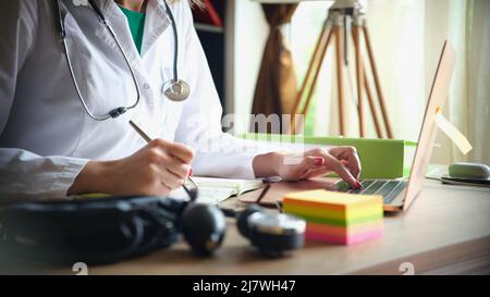 Medico femminile in camice di laboratorio lavora e prende appunti di informazioni sul paziente Foto Stock