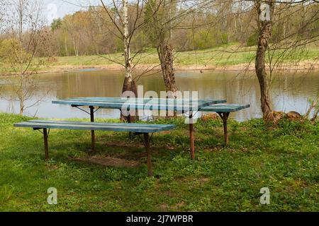Un tavolo e due panchine in legno sulla riva del fiume Foto Stock