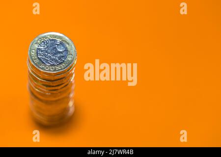 Una pila di monete in sterline britanniche sparate dall'alto con particolare attenzione alla moneta superiore. Questo denaro è fotografato su uno sfondo arancione luminoso e colorato Foto Stock