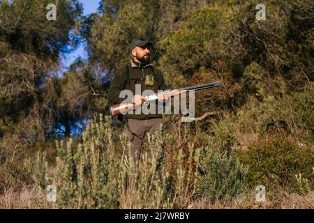 Uomo adulto che tiene la sua pistola in mezzo alla natura guardando via Foto Stock
