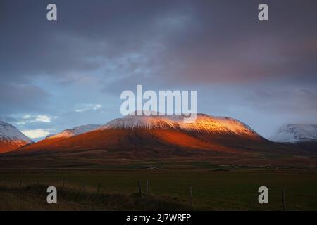 Montagne innevate con campo piano e cielo grigio durante l'ora d'oro vicino a Varmahlíð, Islanda settentrionale Foto Stock