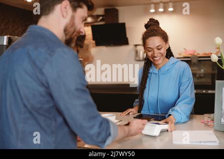 Cliente maschile in caffetteria a pagamento per il caffè al banco. Barista donna che vende bevande al bar. Posteriore. Foto Stock