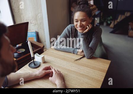 Bella giovane donna felice in amore guardando l'uomo mentre si siede al tavolo in caffetteria. Informazioni sulla data. Foto Stock