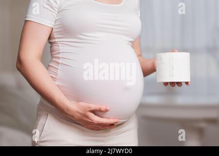 Carta igienica nelle mani di una donna incinta, scatto in studio, soggiorno a casa Foto Stock