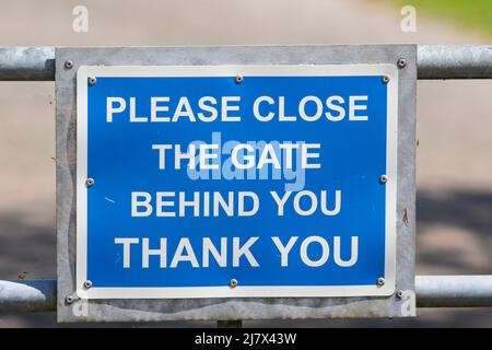 Cartello "Please Close the Gate Behind You", UK Countryside. Avviso gentile per escursionisti e bastioni utilizzando sentiero di campagna vicino a terra privata. Foto Stock