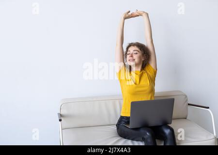 Felice soddisfatto utente laptop donna rilassarsi su un comodo e spazioso divano, stretching corpo godere a casa il tempo libero, sentirsi bene, stress sollievo Foto Stock