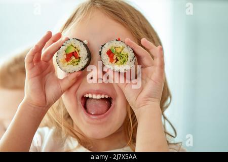 Ragazza piccola divertente che tiene sushi rotolini davanti agli occhi su sfondo bianco Foto Stock