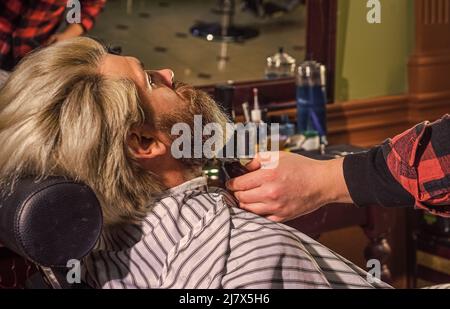 Mantenere la forma della barba. Fai crescere barba e baffi. Uomo al barbiere. Salone parrucchiere. Barbiere e cliente professionali. Rifinire la barba da vicino Foto Stock