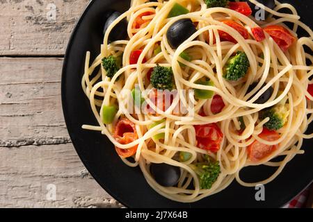 Spaghetti con verdure (broccoli, pomodori, peperoni) su tavola di legno Foto Stock