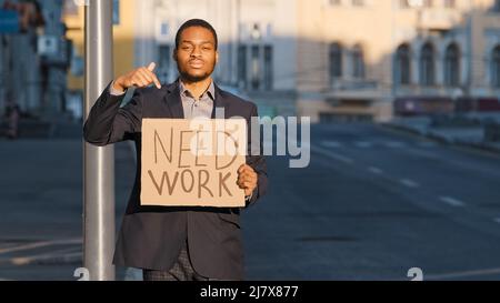 Misto Race businessman in possesso di segno bisogno di punti di lavoro indice dito. Ritratto di giovane uomo in piedi poster di tenuta all'aperto. Maschio sparato bianco millenario Foto Stock