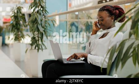 Giovane ragazza freelancer business donna capo femmina capo seduta sul divano in azienda ufficio parlare telefono negoziati digitando sul laptop opere on-line Foto Stock