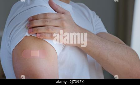 Corto tiro arabo giovane uomo, ritratto maschio spagnolo etnia paziente guardando la spalla con cerotto medico sul segno di iniezione sorridente Foto Stock