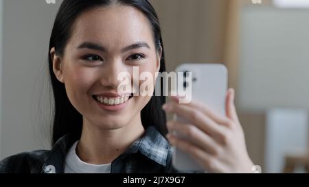 Felice asian coreano giapponese cinese ragazza sorridente femmina viso donna con telefono cellulare che ondeggiano mano parlare con la webcam fare videochiamata a casa parlare Foto Stock