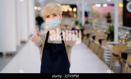 Donna proprietario di piccola impresa ristorante caffetteria adulto bionda donna con capelli corti cameriera indossare grembiule e medico volto guardando la macchina fotografica Foto Stock