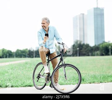 uomo anziano smartphone bicicletta bicicletta cellulare cellulare telefono cellulare all'aperto parco città business casual business Foto Stock