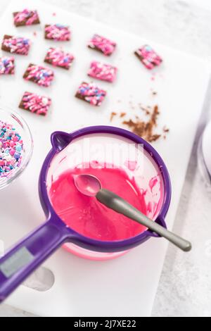 Il cioccolato rosa fuso a gocce sopra i mini cioccolatini e spruzzando alcuni spruzzi colorati sulla parte superiore. Foto Stock