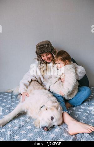 Mamma e figlia coccolano comodamente a casa con il loro animale domestico Labrador Retriever Foto Stock