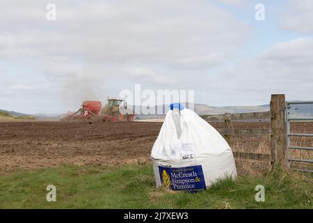 Un sacco di semi all'ingresso di un campo arato con un trattore e seminatrice che operano in background Foto Stock