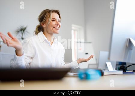 Piacevole donna d'affari che parla alla videochiamata mentre si siede sul posto di lavoro in ufficio Foto Stock