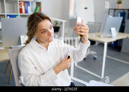 Bella donna matura con mascara in mano si guarda nello specchio Foto Stock