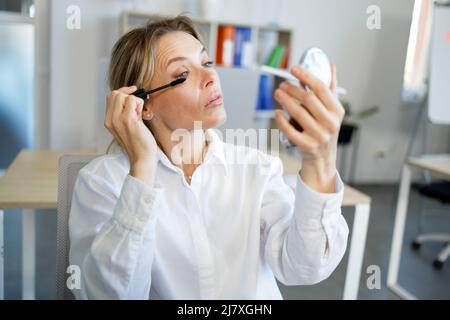 Donna d'affari di mezza età in abbigliamento formale che applica mascara Foto Stock