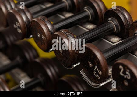 File di manubri di ferro su una rastrelliera in palestra, vecchi e consumati con i numeri di peso su di loro Foto Stock