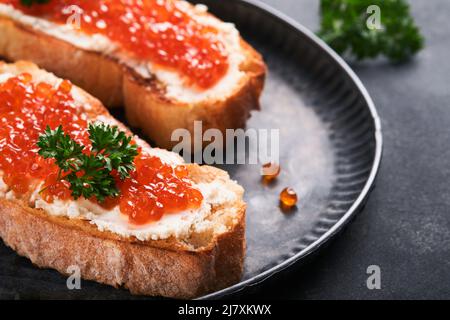 Due dandwiches con caviale rosso. Caviale rosso salmone in ciotola e sandwich server su vecchio piatto di ferro su sfondo vecchio tavolo nero. Vista dall'alto. Spazio di copia. Foto Stock