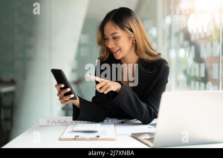 Donna asiatica d'affari che sventolano fisti, ha ottenuto buone notizie sullo smartphone mobile in ufficio, social media network, videochiamate, comunicazione. Foto Stock