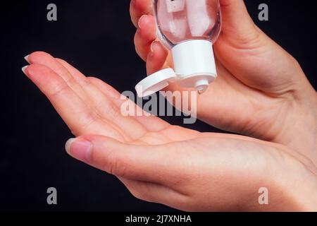 Le mani umane usano un gel, disinfettante, antisettico in una bolla, vaso su uno sfondo nero Foto Stock